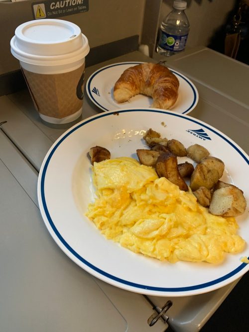 eggs and potatoes with a croissant and coffee on a train tray