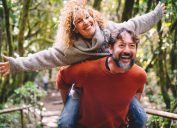 Overjoyed adult couple have fun together at outdoor park in leisure activity. Man carrying woman in piggyback and laugh a lot. Love and life mature people lifestyle concept. Enjoying vacation nature