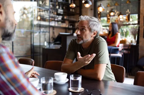 Two middle aged male friends sitting in a coffee shop, having an important conversation over a cup of coffee
