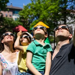 A family with young children watching a solar eclipse while wearing protective glasses