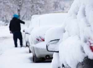 parked cars in the snow in the morning after a blizzard, the driver cleans the snow from his car, Ukraine Dnipro