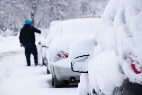 parked cars in the snow in the morning after a blizzard, the driver cleans the snow from his car, Ukraine Dnipro