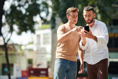 Excited man showing social media profile picture of his new girlfriend to friend when they are walking in park