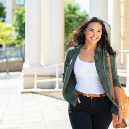 A smiling young woman wearing a casual outfit walks outside.