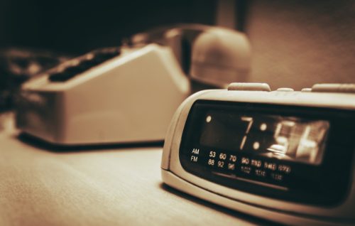 Vintage Hotel Room alarm Clock and the Analog Phone Close Up. Sepia Color Grading.