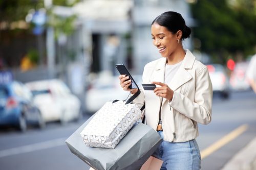 Happy woman with her phone, credit card and bag after shopping in the city. Young latin female carrying bags, spending money, looking for sales and enjoying online eCommerce store sale with a smile