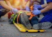 A close up of an injured person's feet lying on a road as they're loaded onto a a stretcher board by EMTs