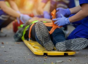 A close up of an injured person's feet lying on a road as they're loaded onto a a stretcher board by EMTs
