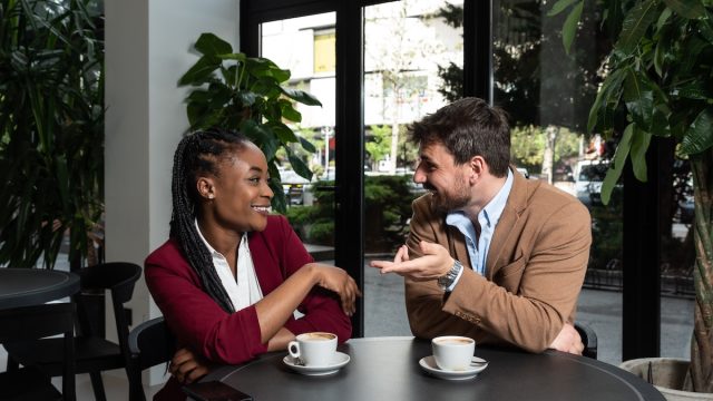 Young man and African American woman sitting in cafeteria drinking coffee flirting
