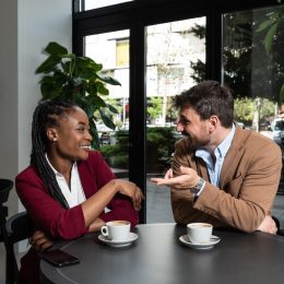 Young man and African American woman sitting in cafeteria drinking coffee flirting
