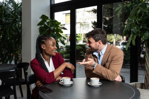 Young man and woman sitting in cafeteria drinking coffee flirting