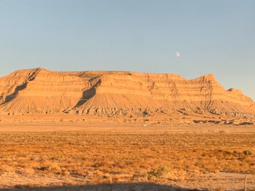 a mesa in utah with the moon above it