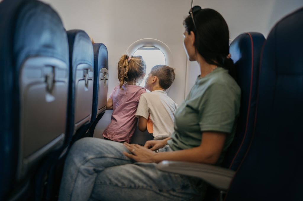 A mother watching her two children as they look out the window of a plane