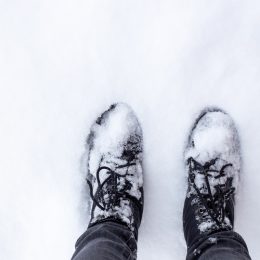 feet in black boots on snowy ground. The arrival of winter and snowy weather.