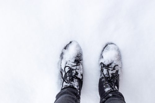 feet in black boots on snowy ground. The arrival of winter and snowy weather.