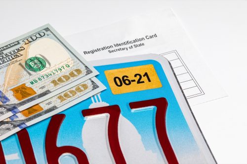 Vehicle license plate, renewal sticker, cash money and registration card. Concept of state government automobile fees, transportation taxes and funding