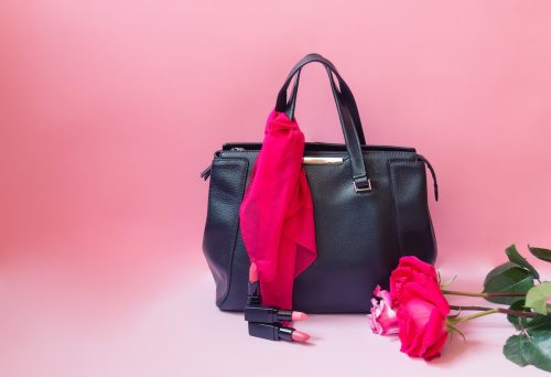 Black leather bag, pink scarf, lipsticks and roses on pink background. 
