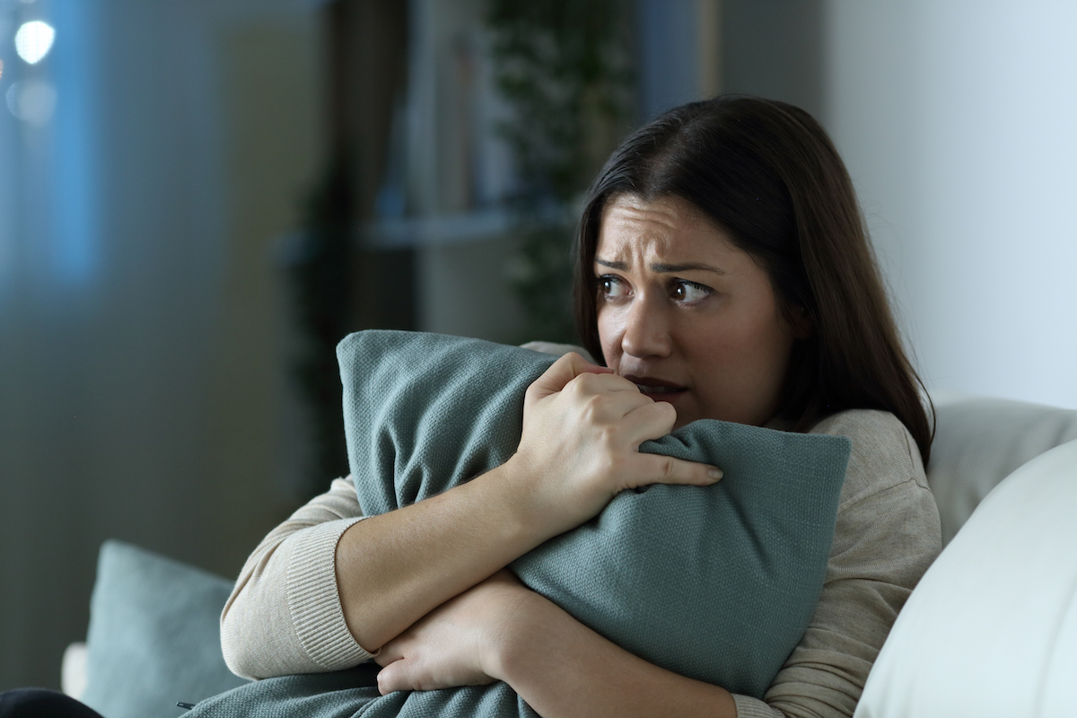 Scared woman embracing pillow in the night sitting on a couch in the living room at home