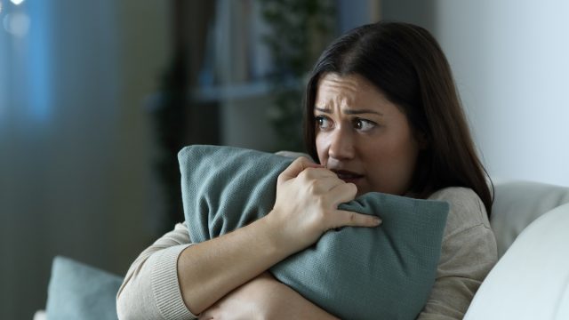 Scared woman embracing pillow in the night sitting on a couch in the living room at home