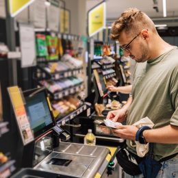 Man buying and paying money in the supermarket. Photo with people in the store during the shopping. Person is using contactless payment