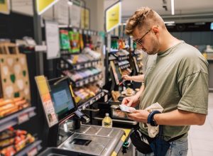 Man buying and paying money in the supermarket. Photo with people in the store during the shopping. Person is using contactless payment