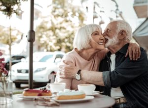 A happy senior couple kissing while sitting at an outdoor cafe with cake on the table