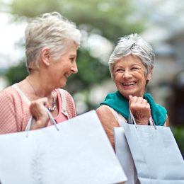 Two senior female friends holding shopping bags and smiling at each other.