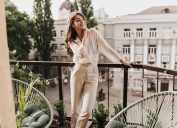 Stylish young woman on balcony in beige neutral outfit with blouse and high-waisted trousers