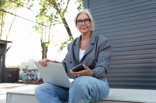Senior business woman working from home with glasses, gray blazer, and laptop