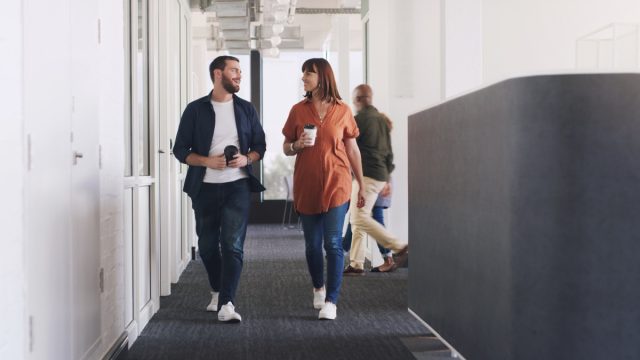 Shot of two businesspeople drinking coffee while walking through a corridor in an office together