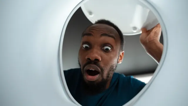 Looking up at a surprised man peering into his toilet bowl