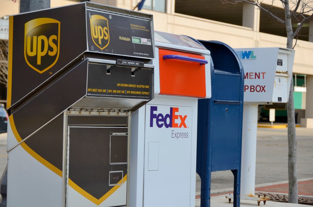 A UPS, FedEx, and USPS box next to each other on the street