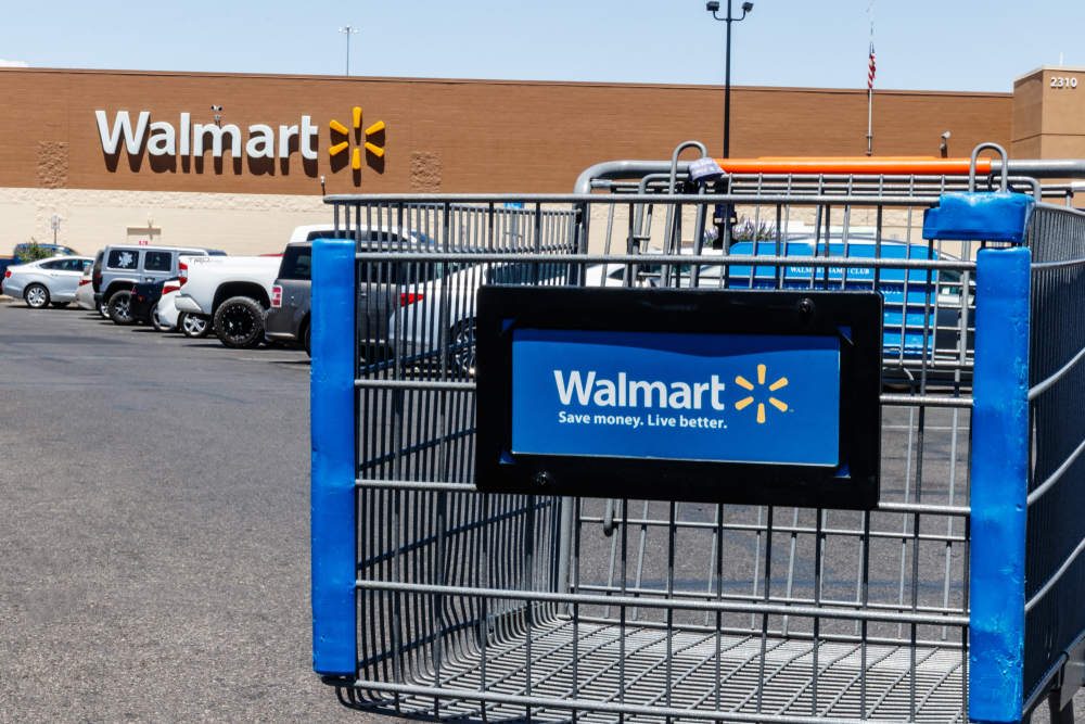 A close up of a Walmart shopping cart in the parking lot in front of a Walmart store