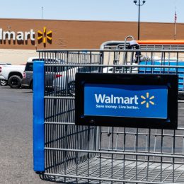 A close up of a Walmart shopping cart in the parking lot in front of a Walmart store
