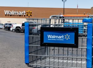 A close up of a Walmart shopping cart in the parking lot in front of a Walmart store