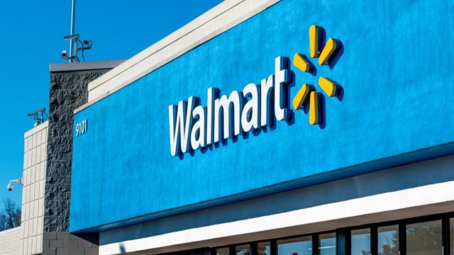 Charlotte, NC USA – December 18, 2022:  Horizontal, medium closeup of "Walmart" superstore's exterior facade brand and logo signage above reflective glass windows and entrance on a sunny morning.