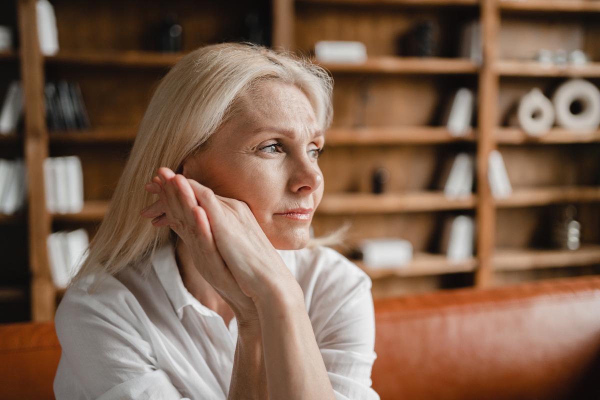 mature woman sitting on couch looking out pensively