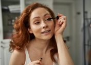 woman with red hair applying mascara in mirror