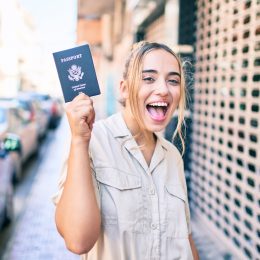 A young woman holding up a passport on the street while smiling