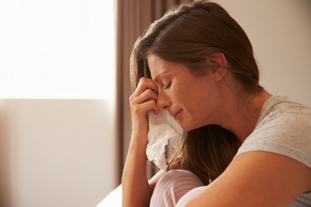 A young woman sitting on her bed with her knees to her chest crying.
