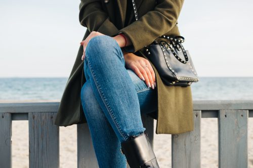 Close-up of a woman in a green coat and jeans sitting on the beach in winter