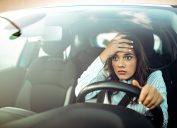 A woman holding her forehead with a stressed look on her face while driving a car