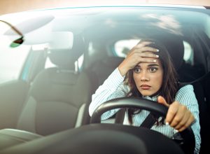A woman holding her forehead with a stressed look on her face while driving a car