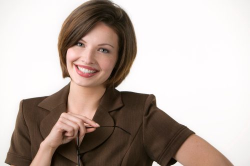 A smiling woman with short brown hair wearing a short-sleeved brown suit smiling at the camera against a white background