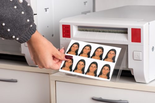 Set of just printed passport photos of a young woman exiting the printer with the hand of a woman reaching for the sheet