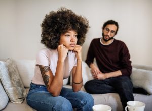 couple in living room drinking coffee or tea and expressing negative emotions