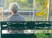 elderly woman depressed and sad sitting back on bench in autumn park.