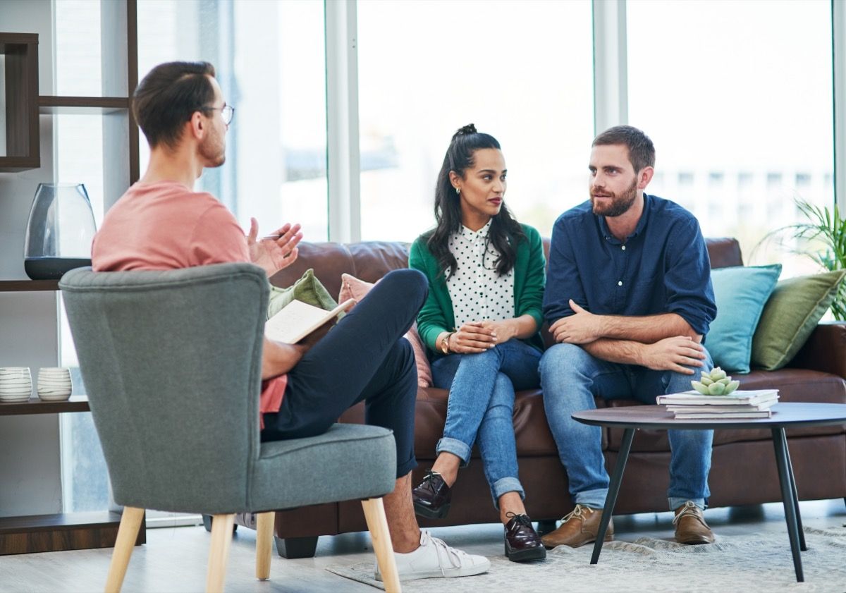 A young couple sitting on a couch in therapy while the therapist sits across from them on a chair