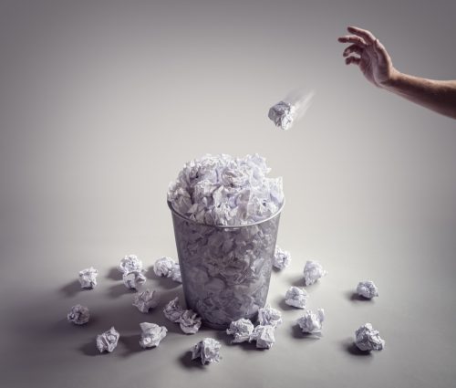 Close up on hand throwing wads of paper into full wastebasket
