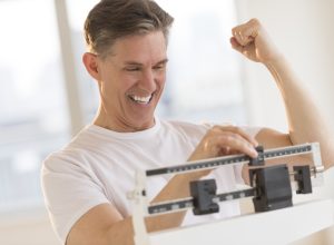 Excited mature man clenching fist while using balance weight scale at gym